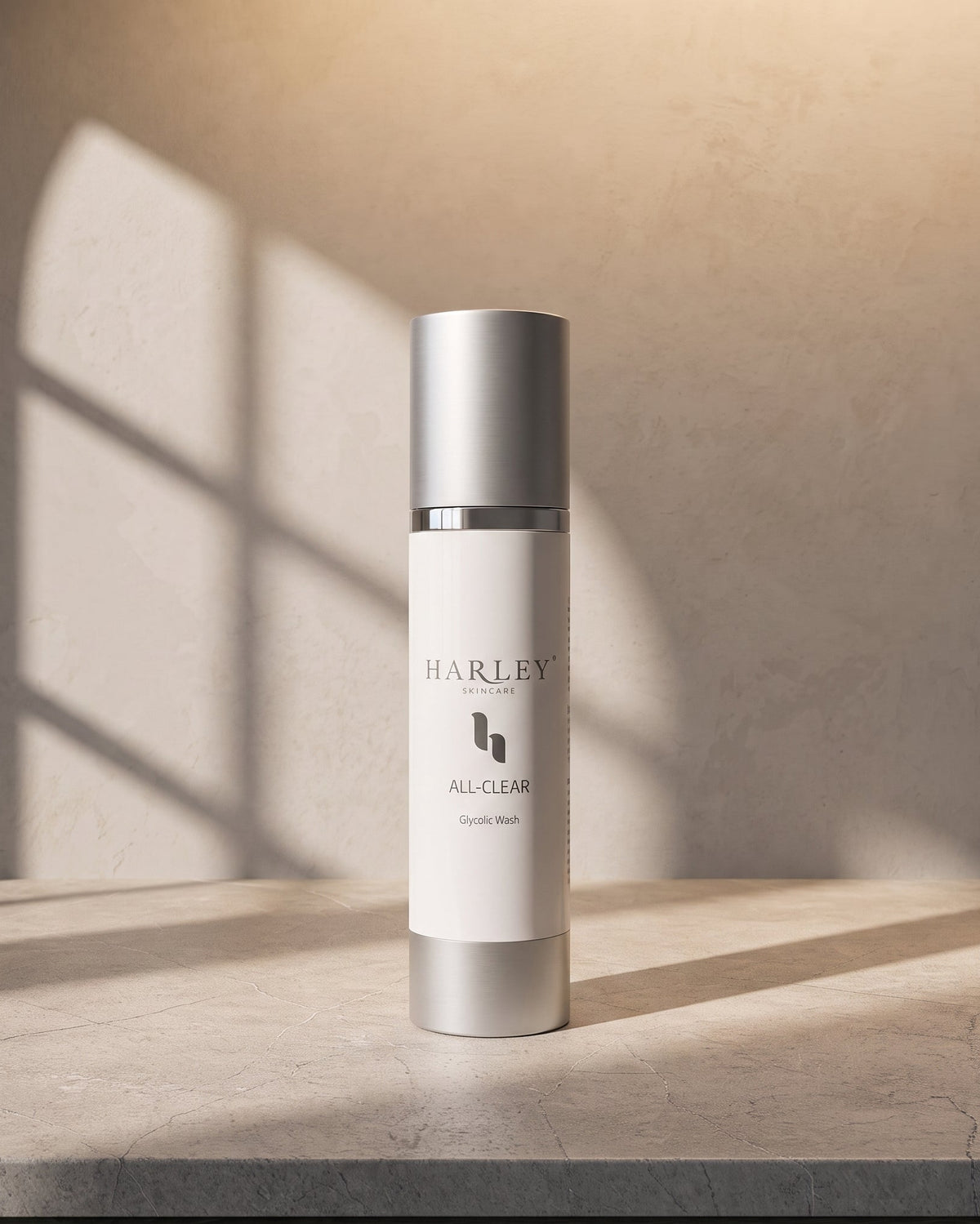 A cylindrical Harley Skincare All-Clear Hydrating Mask bottle with a white body and metallic silver cap, standing on a stone surface with warm sunlight and window shadow patterns on a textured beige wall.