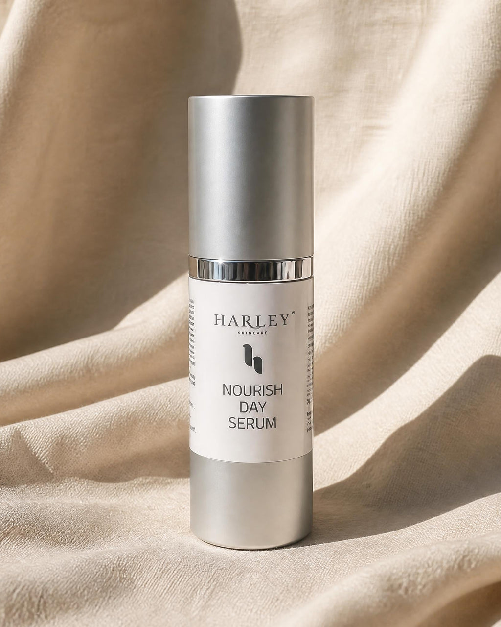 A silver cosmetic bottle of Harley SKINCARE Nourish Day Serum standing upright on draped beige fabric.